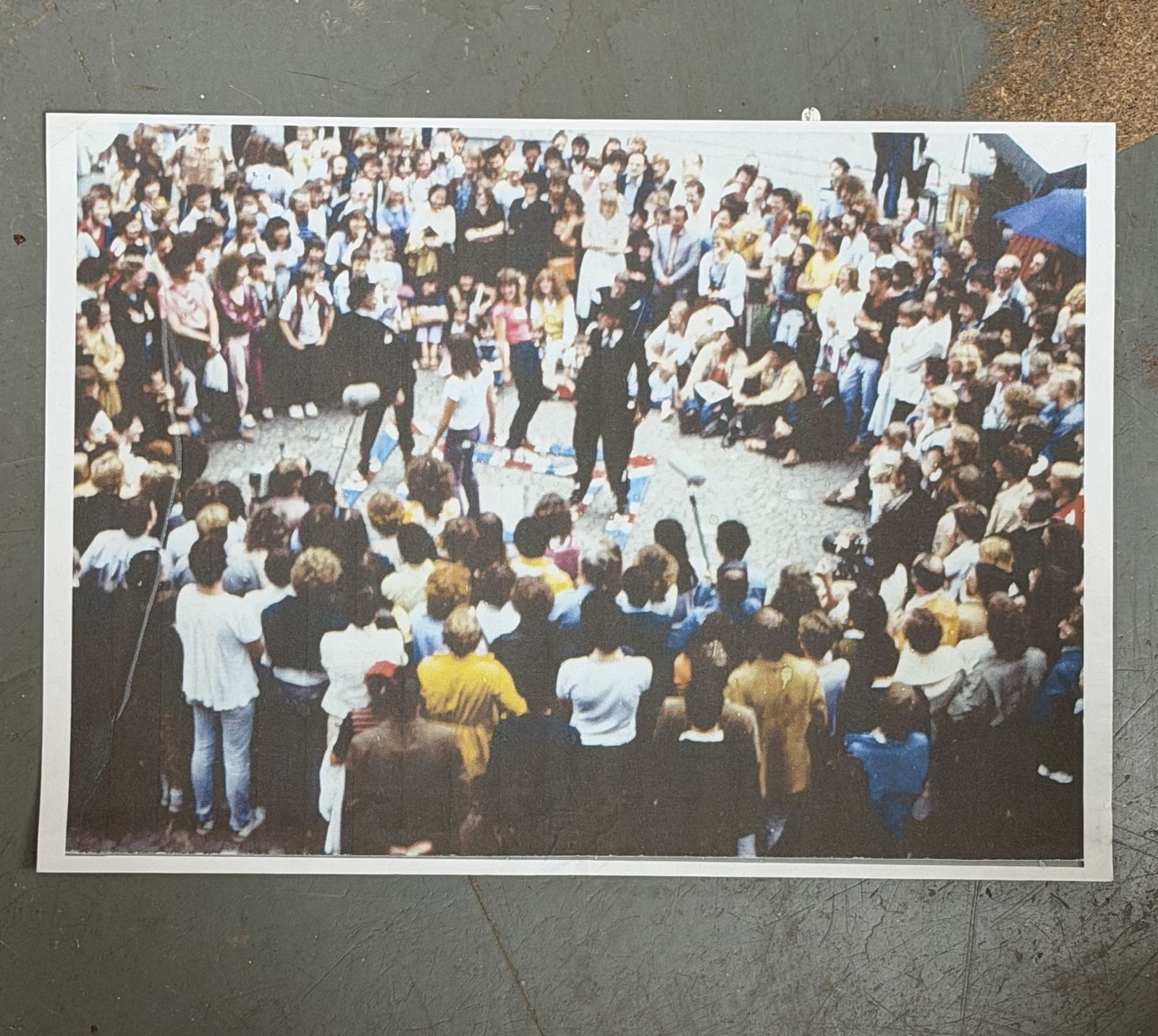 A large street crowd encircling the bowler-hatted square dancers in performance
